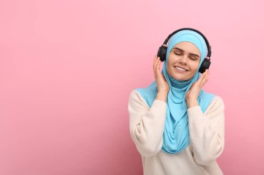Türbanlı ve kulaklıklı Müslüman kadın pembe arka planda müzik dinliyor, mesaj için yer var.