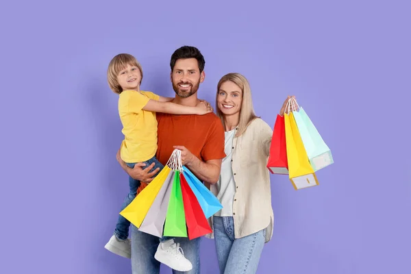 家庭购物 快乐的父母和儿子 背景是紫罗兰色 提着很多彩包 — 图库照片