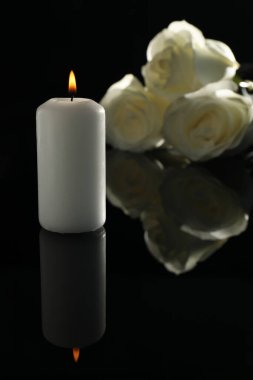 Karanlıkta beyaz güller ve yanan mum siyah ayna yüzeyinde. Cenaze sembolleri