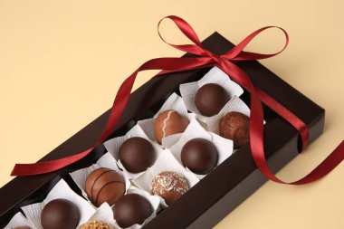 Bej masanın üzerinde lezzetli çikolata şekerleri olan bir kutu, yakın plan.