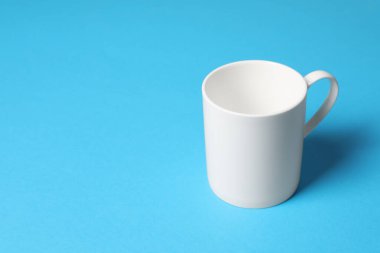 Açık mavi arkaplanda beyaz bir seramik kupa, metin için boşluk