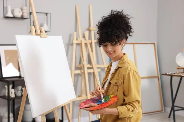 若い女性がスタジオでイーゼルに近いブラシでパレット上の塗料を混合 — ストック写真