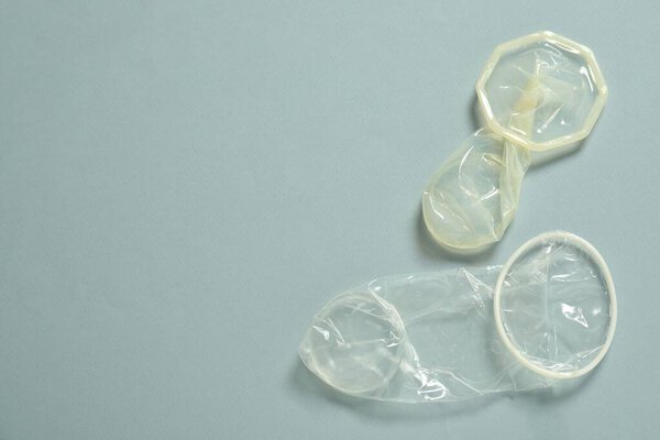 Unrolled female condoms on light blue background, flat lay with space for text. Safe sex