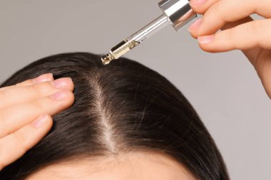 Woman applying essential oil onto hair roots on light grey background, closeup clipart