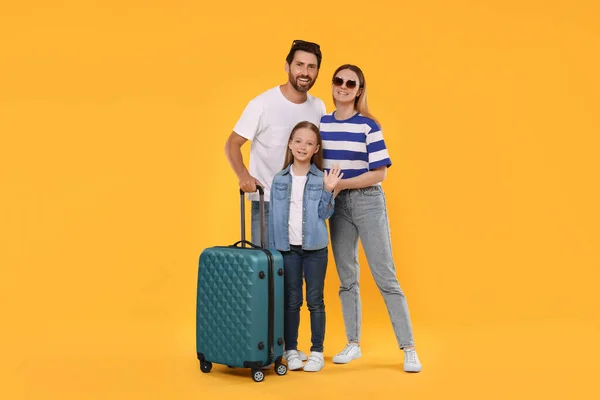 Happy family with green suitcase on orange background