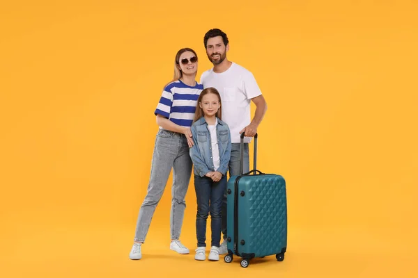 Happy family with green suitcase on orange background