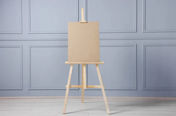 stock image Wooden easel with blank board near grey wall indoors