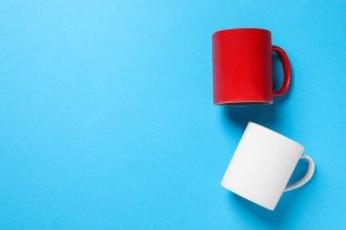 Açık mavi arka planda beyaz ve kırmızı seramik kupalar, düz. Metin için boşluk