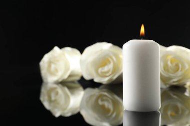 Siyah ayna yüzeyinde beyaz güller ve yanan mumlar karanlıkta, metin için yer ararken yakın çekim. Cenaze sembolleri