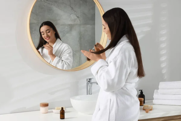 バスルームの鏡の近くで髪にエッセンシャルオイルを塗った幸せな若い女性 — ストック写真