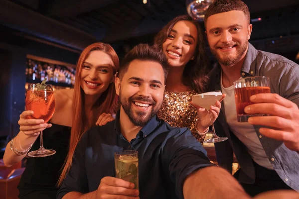 Happy friends with cocktails taking selfie together in bar