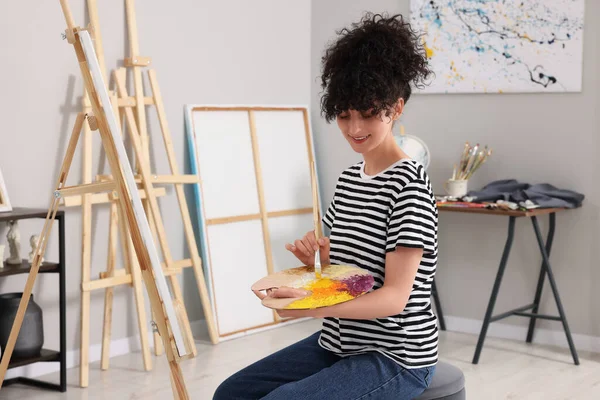 若い女性がスタジオでイーゼルに近いブラシでパレット上の塗料を混合 — ストック写真