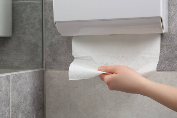 Woman taking new fresh paper towel from dispenser in bathroom, closeup