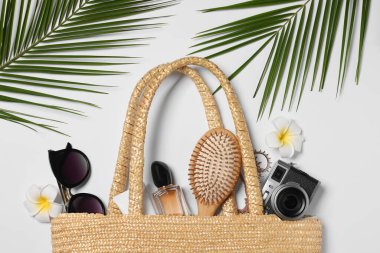 Hasır çanta, palmiye yaprakları ve beyaz arka planda diğer plaj aksesuarları ile düz kompozisyon