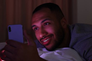 Genç adam gece yatakta akıllı telefon kullanıyor. İnternet bağımlılığı