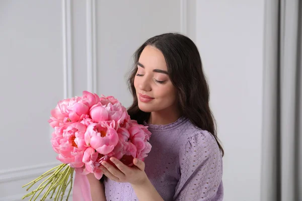 屋内白い壁の近くにピンクの花束が付いている美しい若い女性 — ストック写真