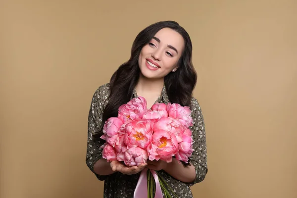ライトブラウンの背景にピンクのコニーの花束を持つ美しい若い女性 — ストック写真