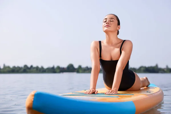 Woman practicing yoga on SUP board on river, space for text