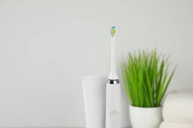 Elektrik diş fırçası ve ışık arka planında yapıştırıcı bulunan tüp.