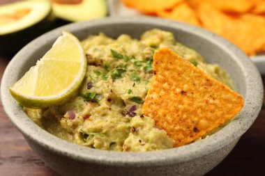 Bir kase lezzetli guacamole, limon ve cips ahşap masada, yakın plan.