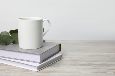Beyaz seramik bardak, kitap yığını ve okaliptüs dalı beyaz ahşap masa, metin için boşluk