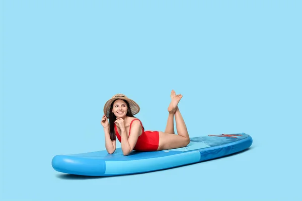 stock image Happy woman resting on SUP board against light blue background