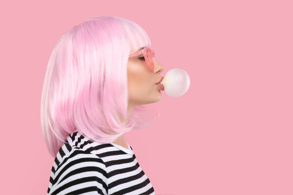 Beautiful woman in sunglasses blowing bubble gum on pink background, space for text