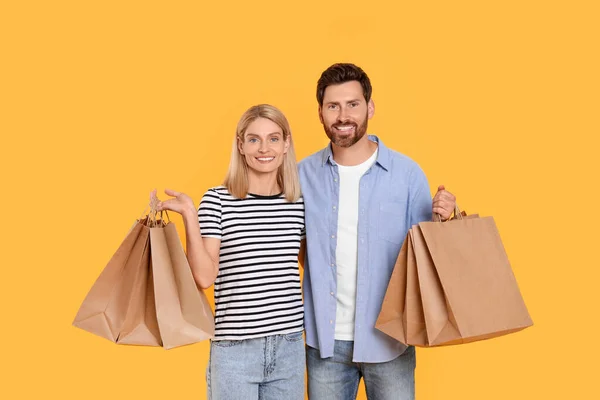ファミリーショッピング オレンジ色の背景に紙袋が付いている幸せなカップル — ストック写真