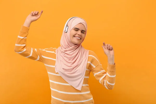 穆斯林妇女头戴头巾 头戴耳机 在橙色背景下跳舞 — 图库照片