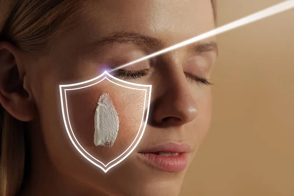 Sun protection care. Beautiful woman with sunscreen on face against beige background, space for text. Illustration of shield as SPF