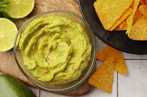stock image Bowl of delicious guacamole served with nachos chips and lime on white tiled table, flat lay