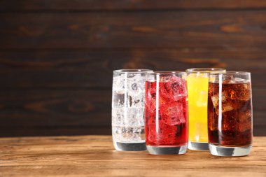 Farklı tazeleyici soda bardakları, ahşap masada buz küpleri, metin için yer.