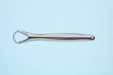 Açık mavi arkaplanda metal dil temizleyici, üst görünüm