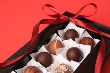 Kırmızı masanın üzerinde lezzetli çikolata şekerleri olan bir kutu, yakın plan.