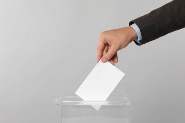 Adam oyunu açık gri arka planda oy sandığına koyuyor, yakın plan. Metin için boşluk