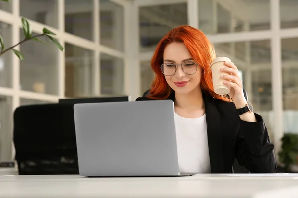 在办公室的白色桌子上 一个快乐的女人拿着纸杯咖啡在笔记本电脑上工作 — 图库照片