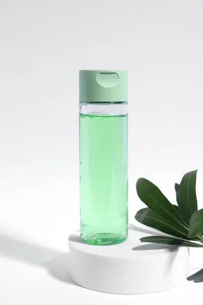 Bottle with cosmetic product and green leaves on white background