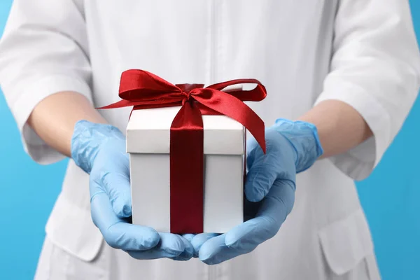 stock image Doctor holding gift box on light blue background, closeup. Medical present