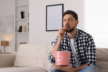 Adam evde kanepede patlamış mısır yerken televizyon izliyor.