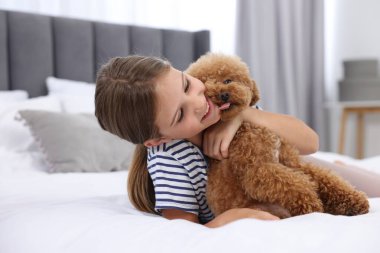 Evde küçük bir çocuk yatakta sevimli bir köpek yavrusuna sarılıyor. Sevimli hayvan