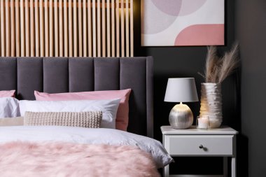 Yastıklı, lambalı ve beyaz komodinli rahat bir yatak. Şık iç mekan