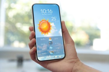 Kadın kapalı mekanda akıllı telefondan hava durumunu kontrol ediyor, kapatıyor. Veri, güneş ve diğer illüstrasyonlar ekranda