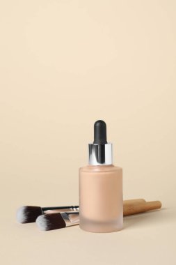 Bir şişe deri temeli ve bej arka planda fırçalar. Makyaj ürünü