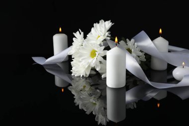 Beyaz kasımpatı çiçekleri ve siyah ayna yüzeyinde yanan mumlar karanlıkta, yazı için boşluk. Cenaze sembolleri
