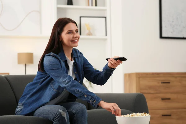 Happy woman changing TV channels with remote control on sofa at home