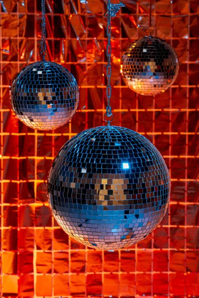 Shiny disco balls against foil party curtain under color lights