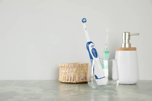 Electric Toothbrushes Glass Toiletries Light Grey Marble Table Space Text — Stock Photo, Image