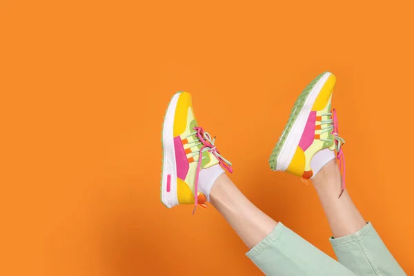 Woman wearing pair of new stylish sneakers on orange background, closeup. Space for text