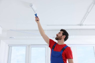Tamirci odada silindirle tavanı boyuyor.