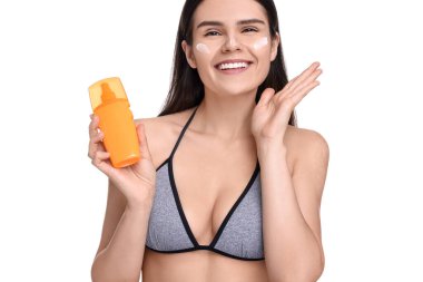 Güzel genç bir kadın beyaz arka planda güneş koruma kremi şişesi tutuyor.